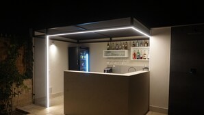 Eine moderne Bar mit einer Theke, Regalen voller Spirituosenflaschen und einem Kühlschrank.