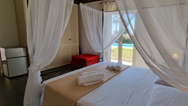 Ein Zimmer mit einem Bett, weißen Vorhängen, einer roten Bank und Blick auf einen Pool.