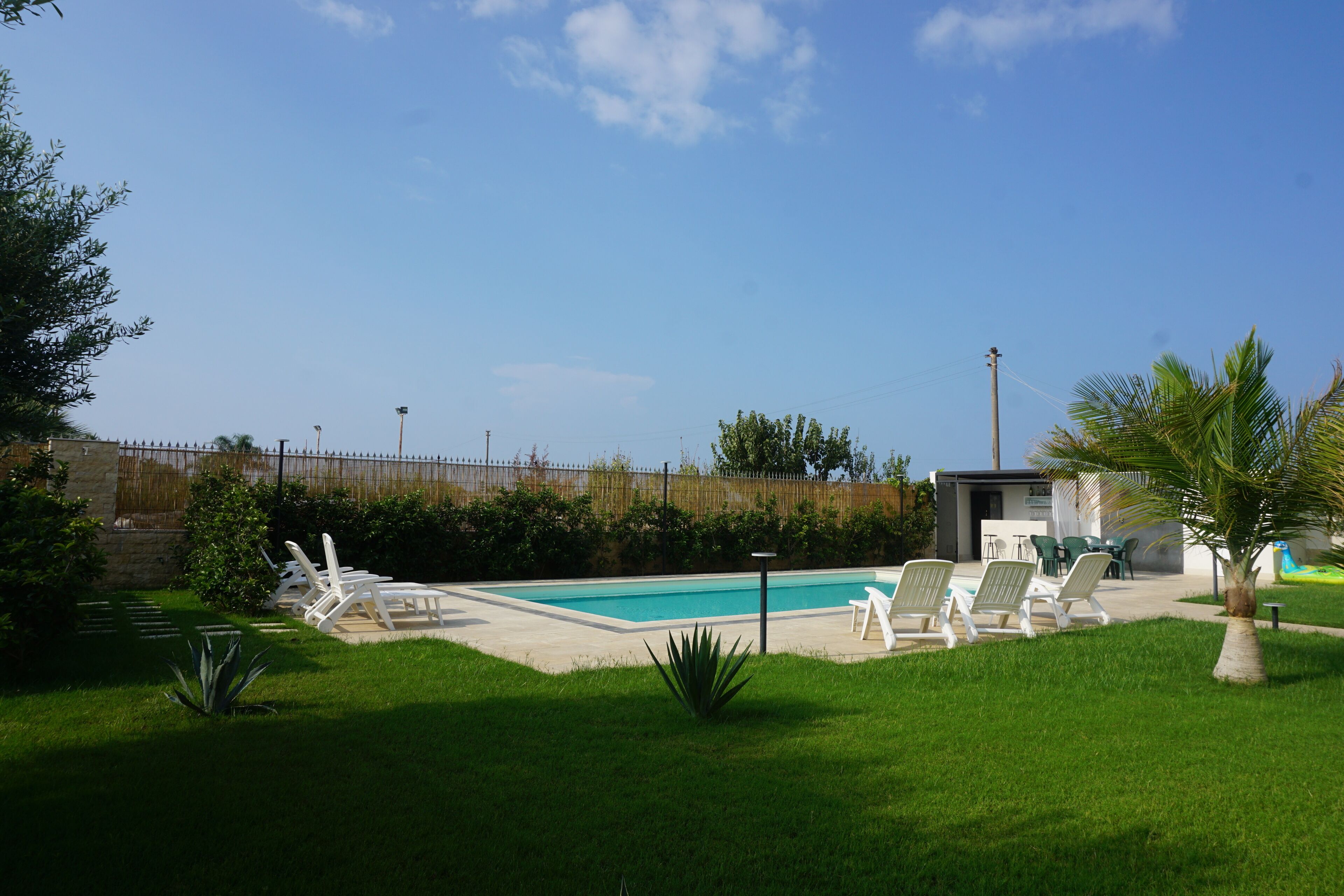 A swimming pool with lounge chairs, a small building, and a fenced area with greenery.
