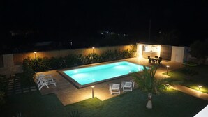 Ein Schwimmbecken mit Liegestühlen und einer kleinen Terrasse bei Nacht.
