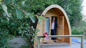 A wooden cabin with an arched entrance, a wooden deck, and a pair of red flowers on the ground. - AN OASIS WHERE TO FIND THE ESSENTIALS<br>AND TAKE A BREAK IN CONSCIOUSNESS & IN (SAINT USUGE)