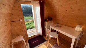 A wooden cabin with a small dining area, a window with curtains, and a view of greenery outside. - AN OASIS WHERE TO FIND THE ESSENTIALS<br>AND TAKE A BREAK IN CONSCIOUSNESS & IN (SAINT USUGE)