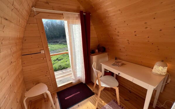 Eine Holzhütte mit einem kleinen Essbereich, einem Fenster mit Vorhängen und Blick ins Grüne.