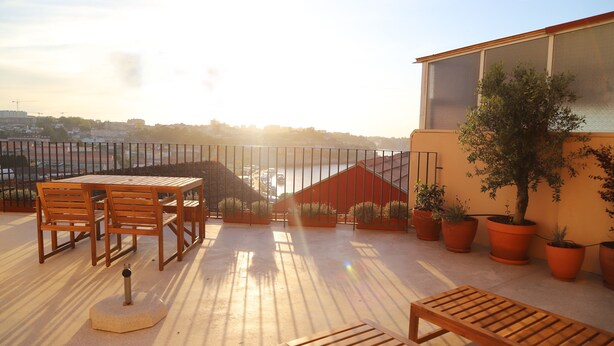 Eine Dachterrasse mit Holztisch und -stühlen, Blumentöpfen und Blick auf die Stadt.