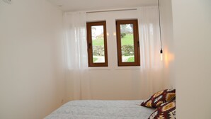 Ein Schlafzimmer mit einem Bett, zwei Fenstern und einer Nachttischlampe.