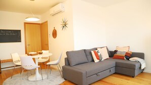 Ein modernes Wohnzimmer mit einem grauen Sofa, weißen Sesseln, einem runden Tisch und einer Holztür.