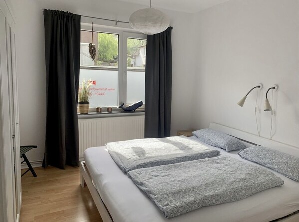 A bedroom with a bed, curtains, a window with a view, and a hanging light fixture.