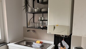 Eine kleine Küche mit Spüle, Herd und einer Arbeitsplatte. Über der Spüle befinden sich Regale mit Geschirr und Einmachgläsern.