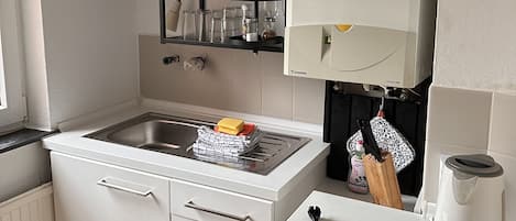 Cozinha com pia, armários brancos, bancada e prateleira com pratos e potes.