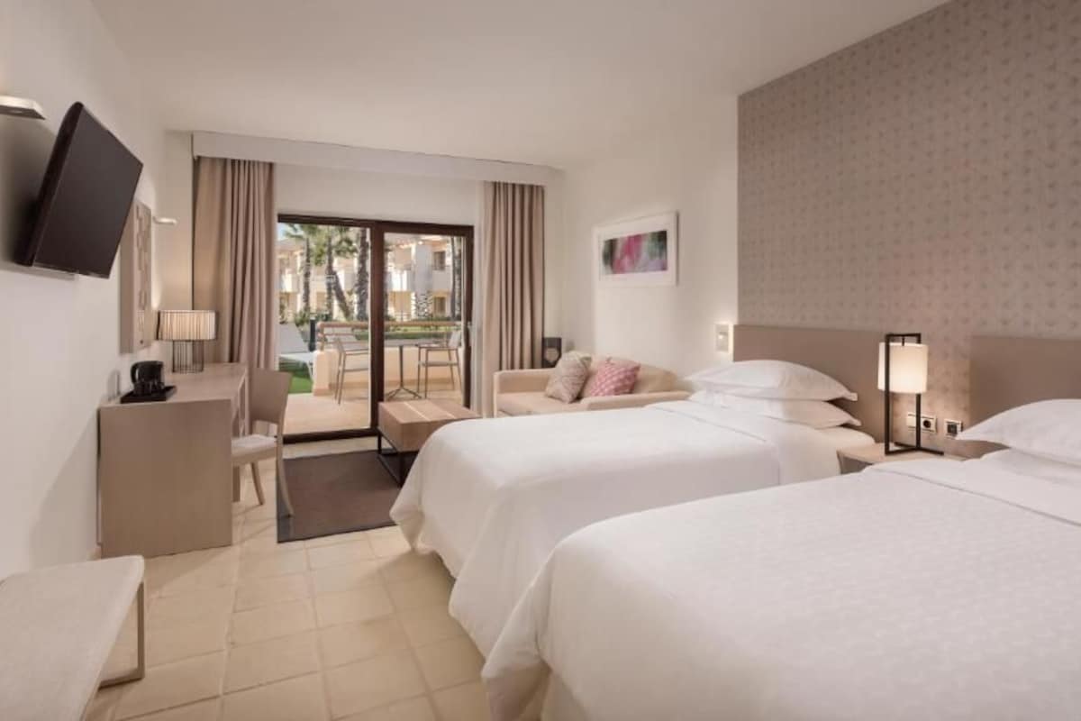Habitación de hotel con dos camas, un escritorio, un televisor y vistas al exterior.