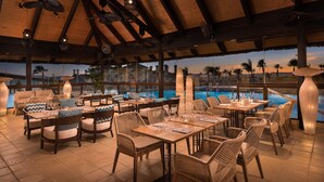 Un restaurant doté de mobilier en osier, offrant une vue sur la piscine et un plafond en bois.