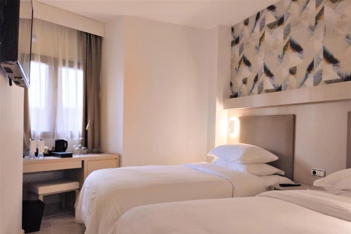 Una habitación de hotel con dos camas, un escritorio con cafetera y un cuadro en la pared.