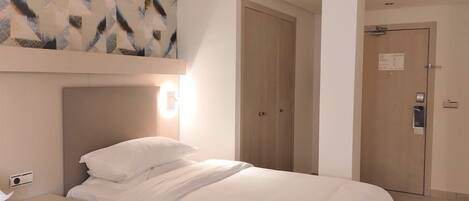 A hotel room with a bed, bedside table, and a wall-mounted light.