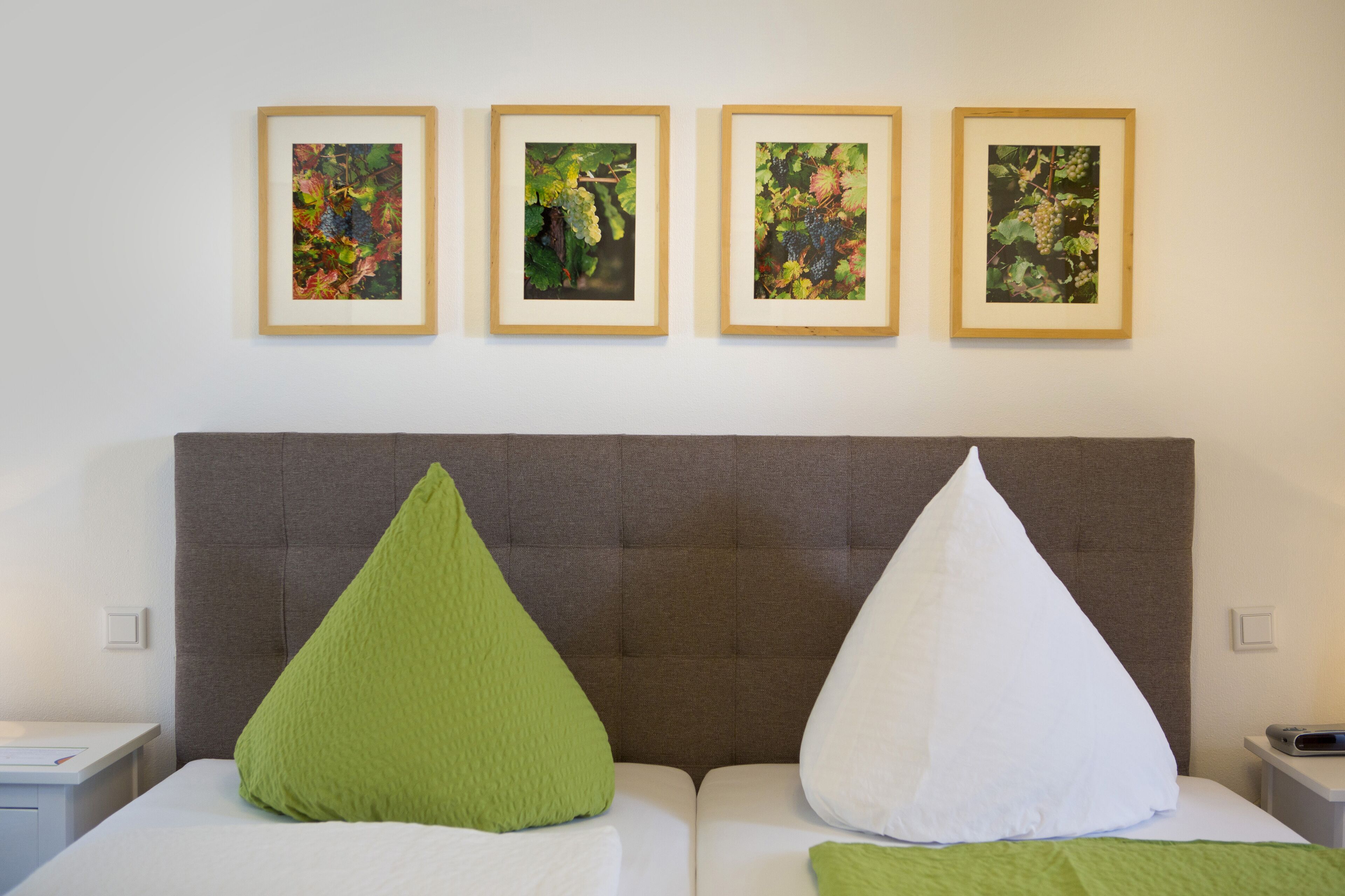 Habitación de hotel con una cama grande, dos almohadas, cabecera y cuatro cuadros enmarcados en la pared.