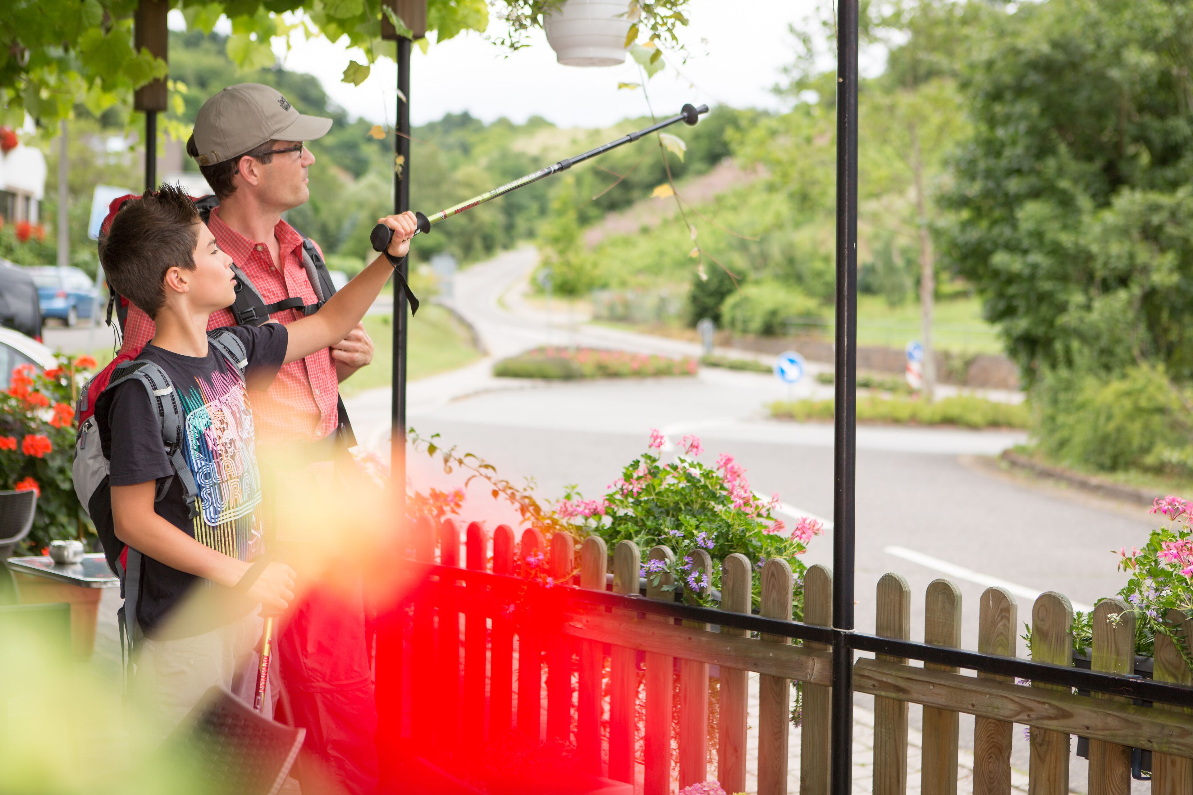 Een man en een kind maken een foto met een camera op een balkon met uitzicht op een weg en groen.