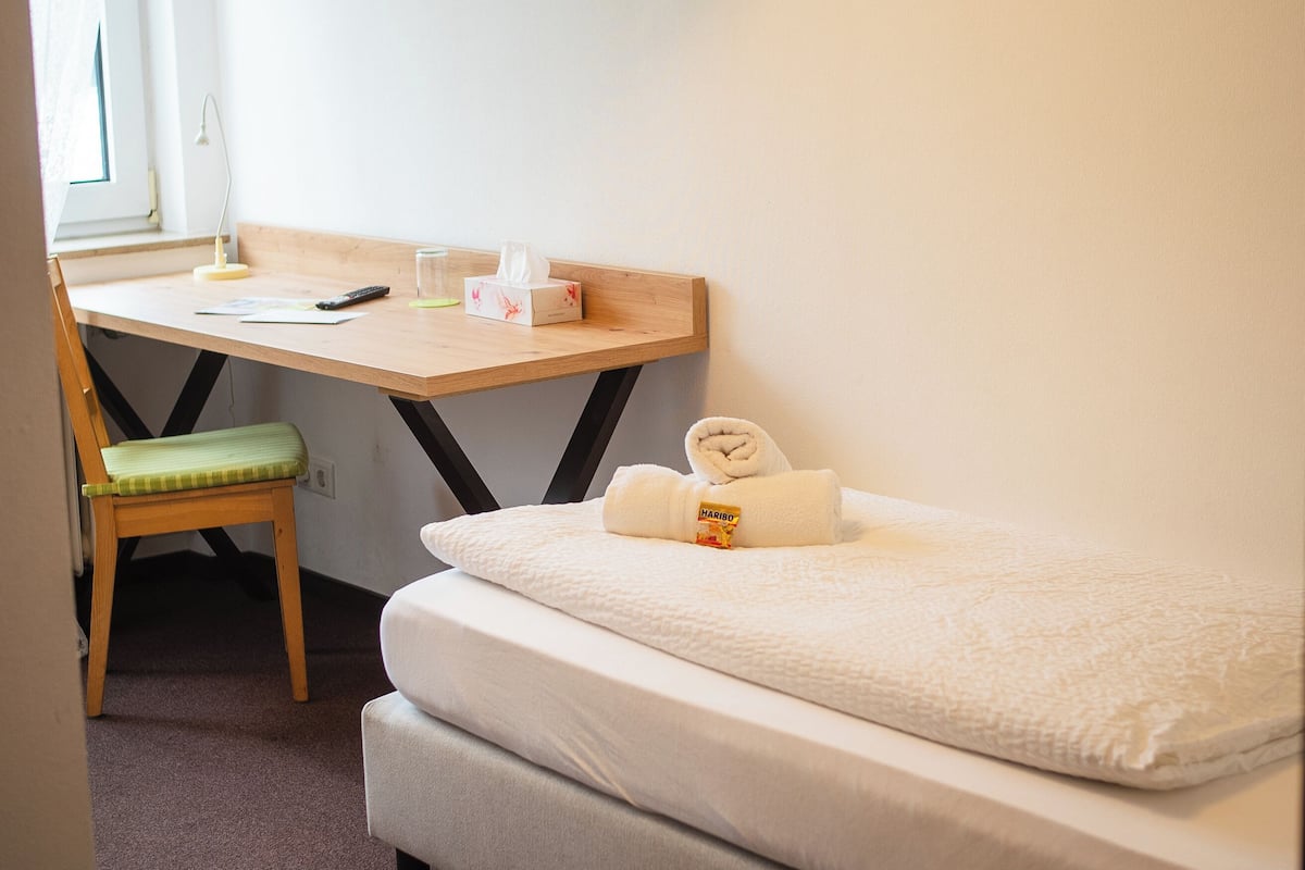 A small, neatly arranged room with a bed, a desk, and a chair.