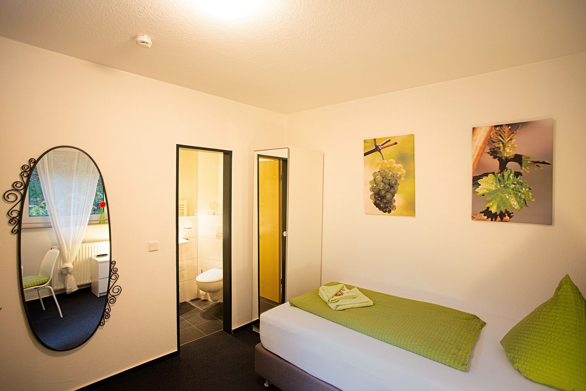 Habitación de hotel con cama, espejo, puerta que da a un baño y dos cuadros en la pared.