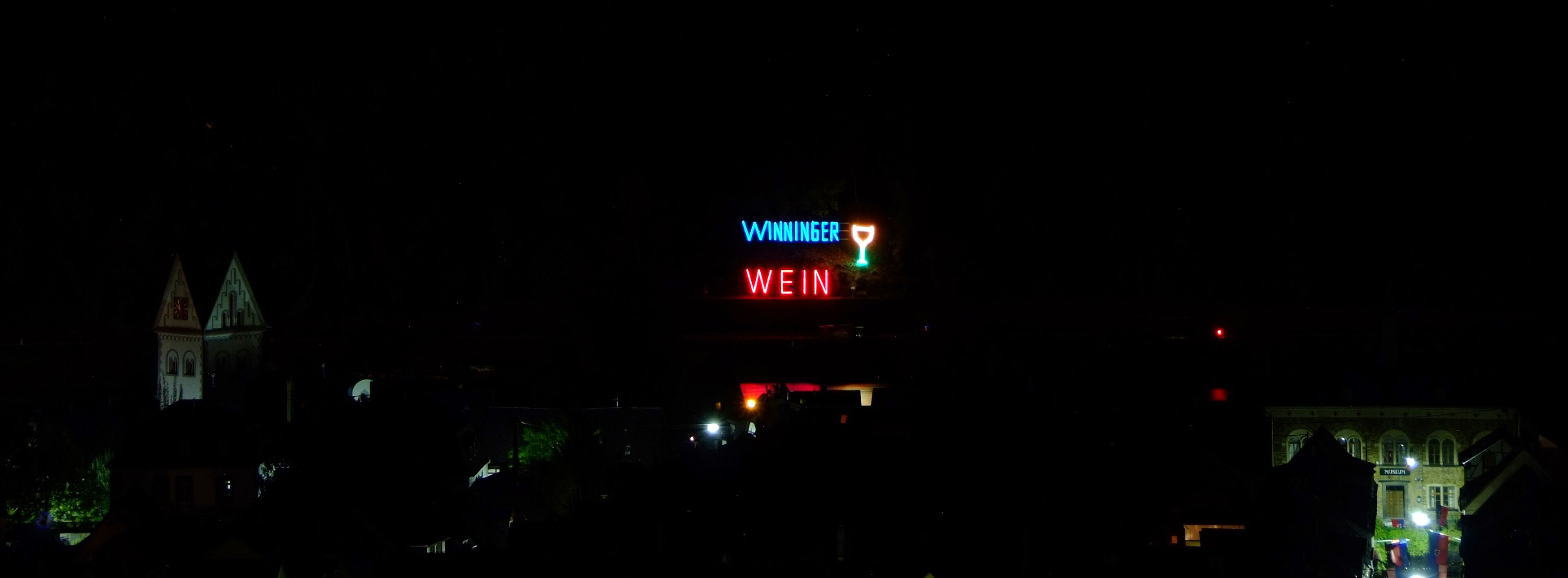 Vista nocturna d'un edifici amb cartells il·luminats que diuen 'WINNINGER WEIN'.