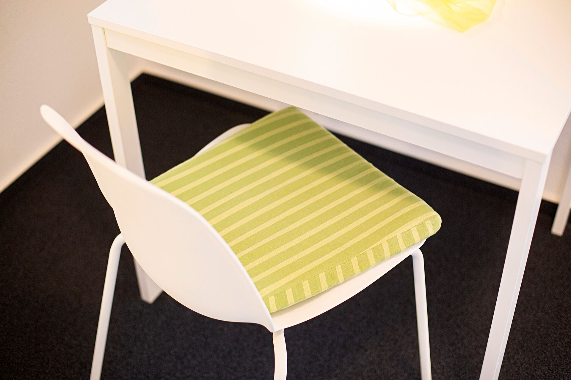 Una silla blanca con un cojín verde a rayas debajo de una mesa blanca.