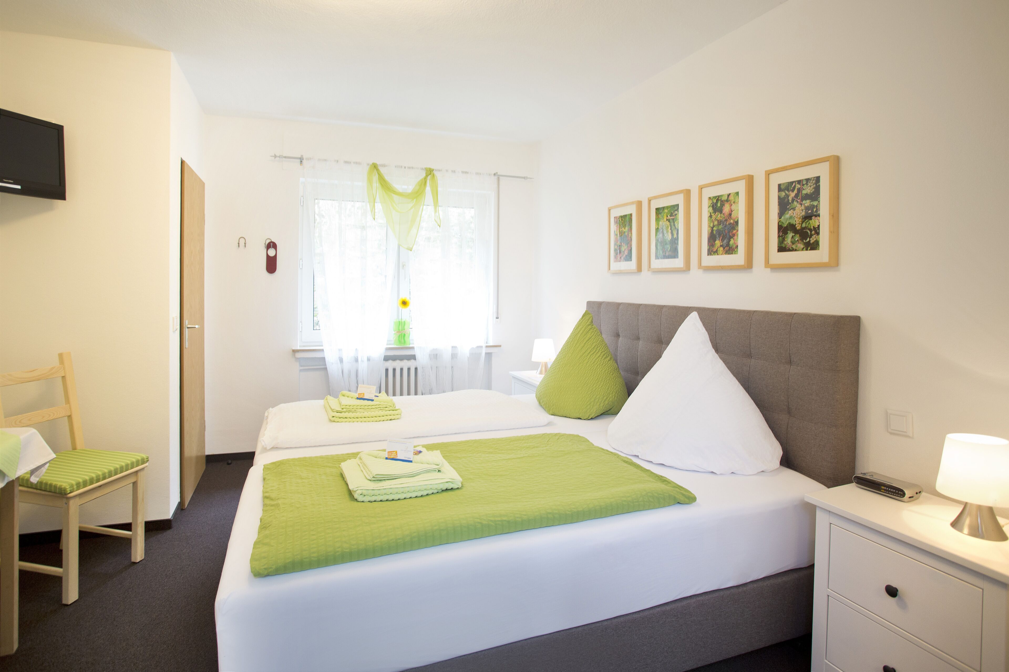 Una habitación de hotel con una cama, una silla, un escritorio, una lámpara y cuadros en la pared.
