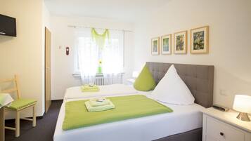 Una habitación de hotel con una cama, una silla, un escritorio, una lámpara y cuadros en la pared.