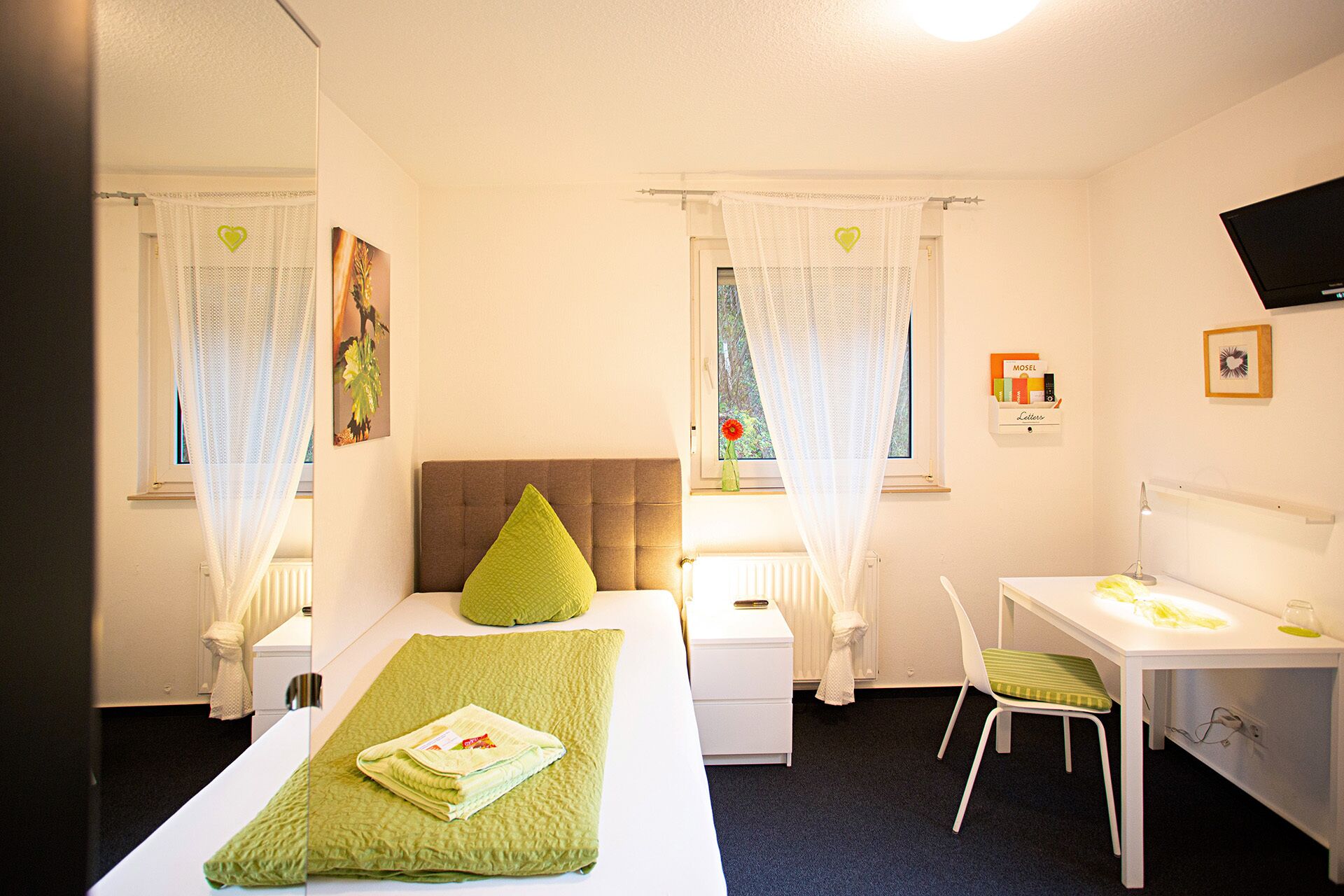A bedroom with a bed, a desk, a chair, a radiator, and a window with curtains.
