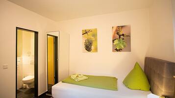 A hotel room with a bed, a green pillow, a green blanket, and two wall art pieces depicting plants.