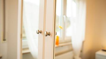 Primer plano de una puerta blanca con manijas plateadas, que da paso a un cuarto con ventana y un área de baño visible.