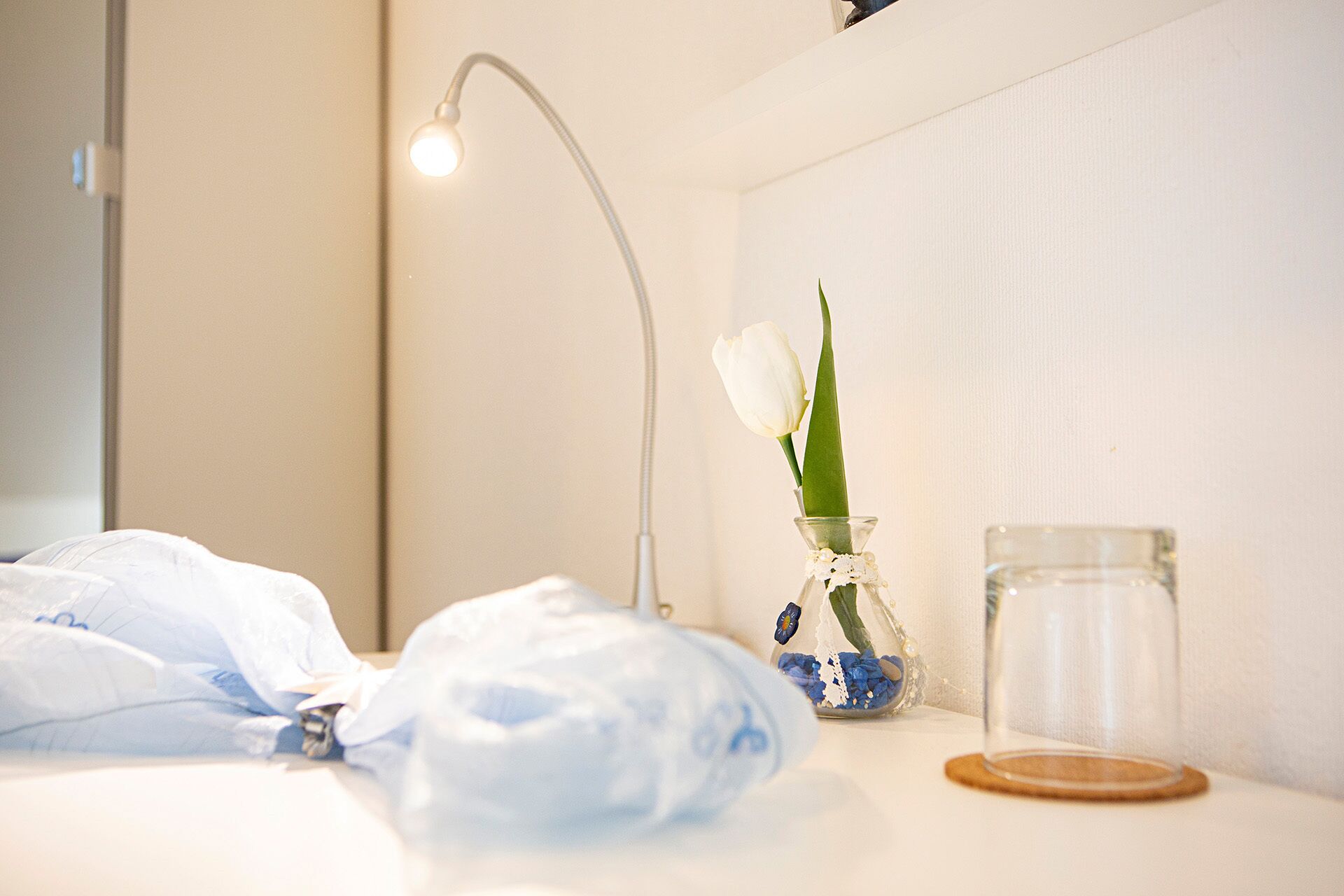 A bathroom with a white sink, a glass vase with a single white tulip, and a clear glass jar.