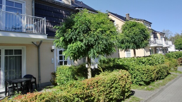 Une rangée de maisons à deux étages, dotées de balcons, et entourées d’arbustes et d’arbres bien entretenus.
