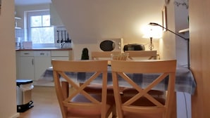 Un coin repas avec une table et des chaises, une lampe, une horloge, et une cuisine en arrière-plan.