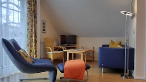 Un salon moderne avec un canapé, un fauteuil, une petite table et un téléviseur.
