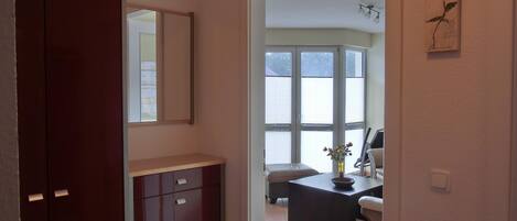 Une pièce avec un meuble en bois, un bureau orné d’un vase et une fenêtre avec des stores.