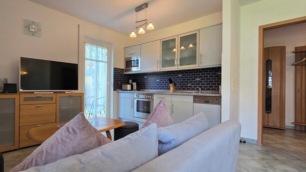 A modern kitchen with a large TV, wooden cabinets, and a dining area with a sofa. - 2-zi-ferwo für 3 Pers im EG. Wlan (Graal-Müritz)