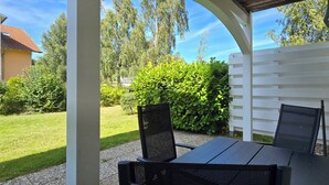 A covered patio with a table and chairs, a white fence, and a well-maintained garden. - 2-zi-ferwo für 3 Pers im EG. Wlan (Graal-Müritz)