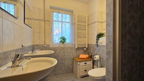 A bathroom with two sinks, a toilet, a window with curtains, a towel rack, and a mirror. - 2-zi-ferwo für 3 Pers im EG. Wlan (Graal-Müritz)
