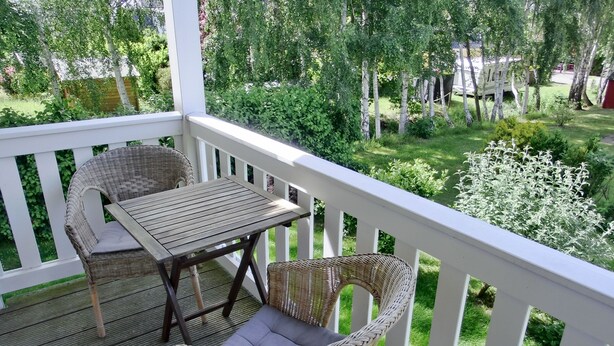 Une terrasse en bois, agrémentée de meubles en osier, notamment une table et deux chaises, donnant sur un jardin luxuriant.