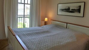 Une chambre à coucher avec un lit, une fenêtre avec des rideaux, une lampe de chevet et un tableau encadré au mur.