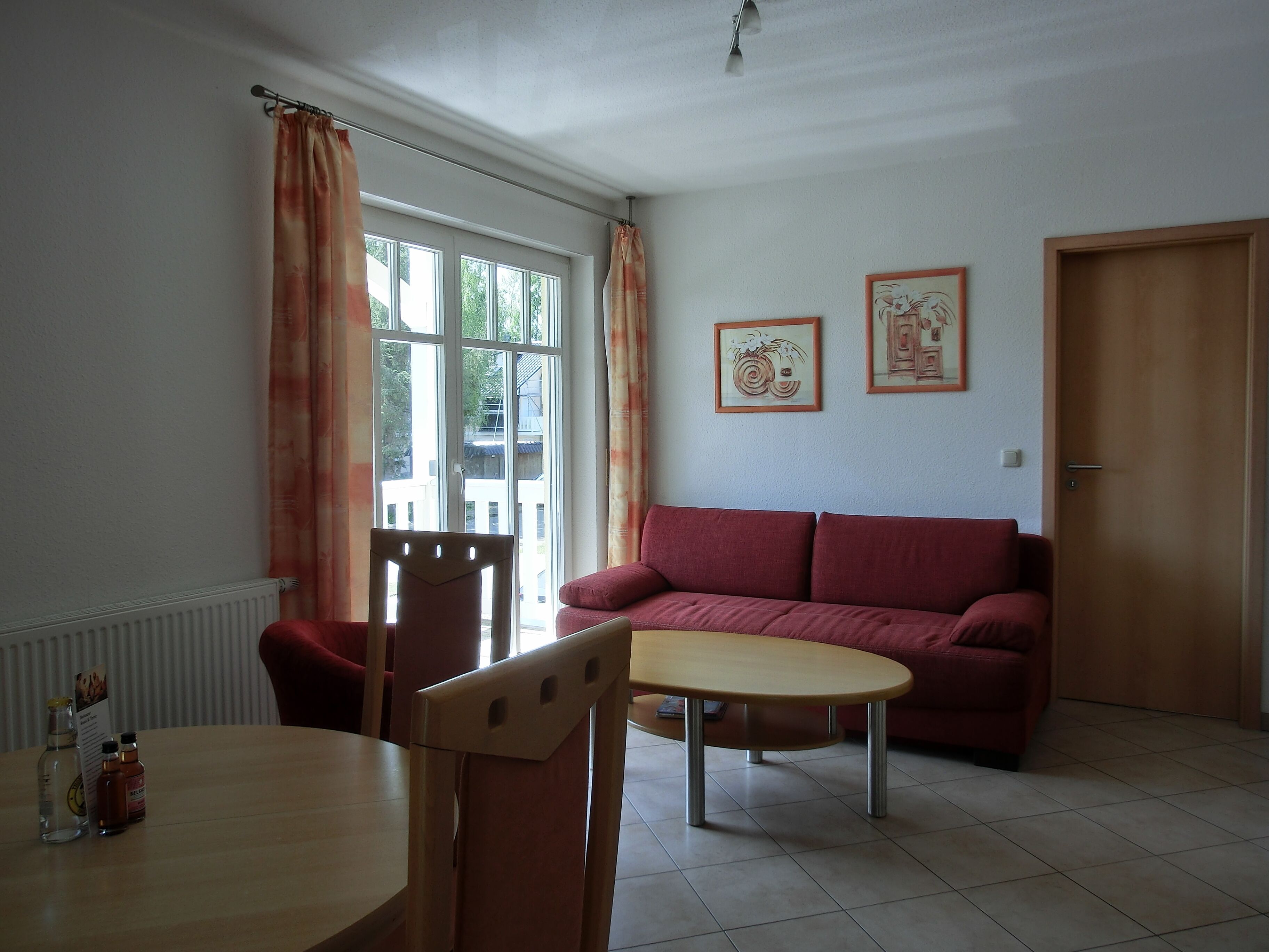 Uma sala de estar com uma mesa de madeira, um sofá vermelho e duas quadros na parede.