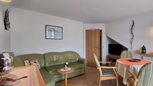 Ein gemütliches Wohnzimmer mit einem grünen Sofa, einem kleinen runden Tisch und einem Fernseher im Hintergrund.