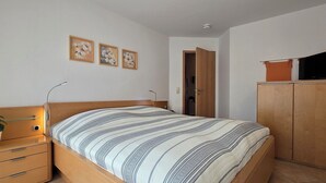 Ein Schlafzimmer mit Bett, Nachttisch mit Schubladen, Lampe, Topfpflanze und Kleiderschrank.