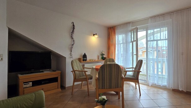 Ein Wohnzimmer mit Fernseher, zwei Sessel, einem Tisch und einem fensterbepflegten Fenster.