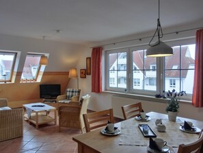 Een gezellige woonkamer met een televisie, comfortabele zithoek en grote ramen met uitzicht op de omgeving.