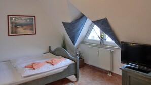 A bedroom with a bed, a painting, a window with curtains, a radiator, and a television.