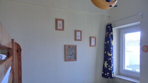 Habitación infantil con una cama litera, un escritorio y una ventana con cortina decorada con motivos lunares y estrellas.