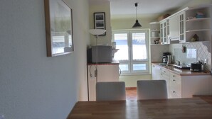 Una cocina con armarios blancos, una mesa de comedor con sillas y una ventana con persianas.