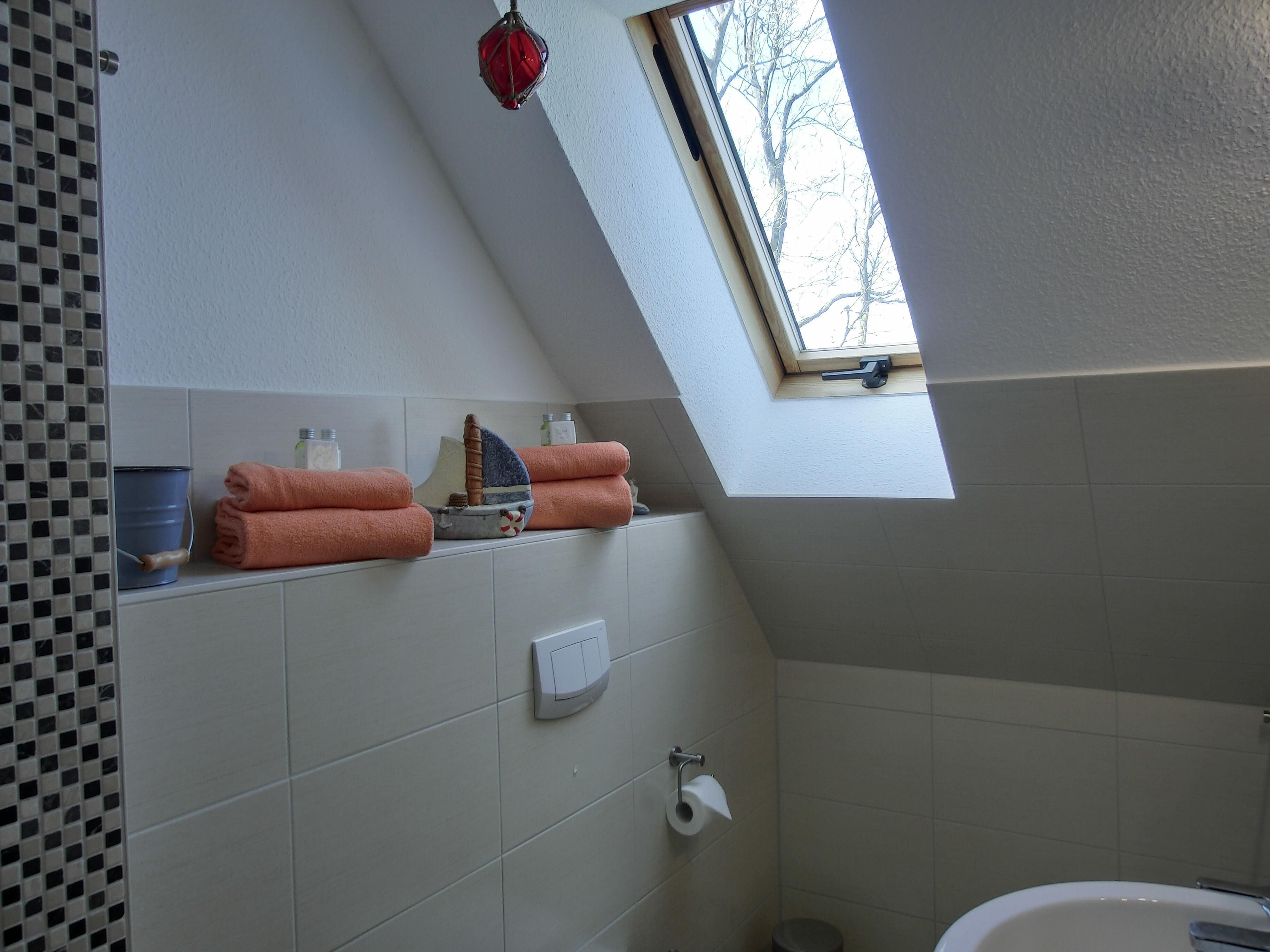 A bathroom with a skylight, a bathtub, a toilet, and a shelf with towels and toiletries.