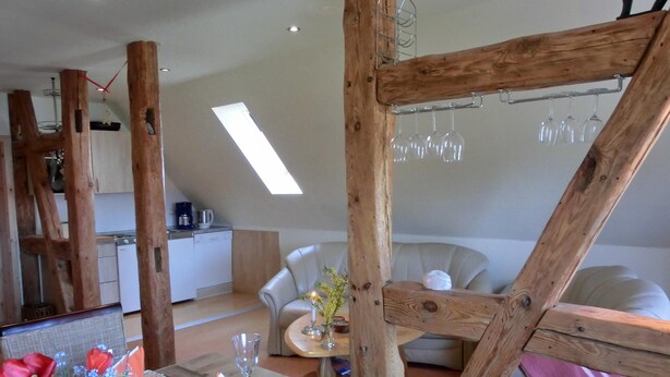 Un comedor con una mesa de madera dispuesta para dos personas, una cocina al fondo y un techo estilo loft con tragaluces.
