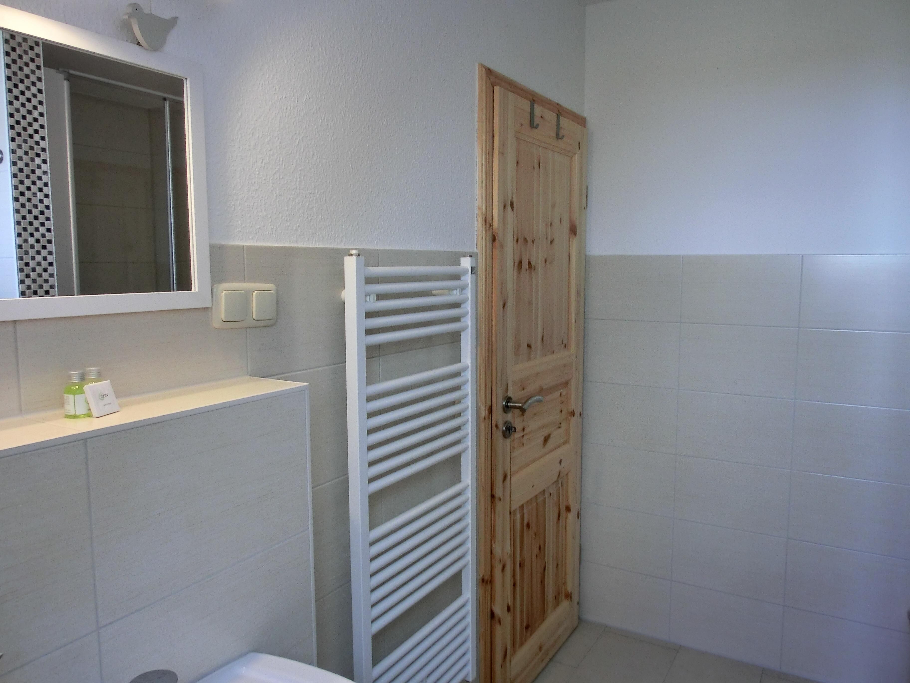 A bathroom with a white tiled wall, a wooden door, a white towel rack, and a mirror above the sink.