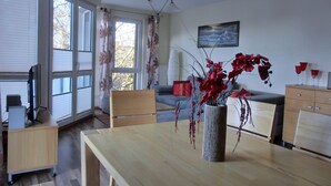 A modern living room with a wooden dining table, a grey sofa, and a red vase with flowers. - 3-room apartment close to the beach for up to 6 people with elevator (Graal-Müritz)